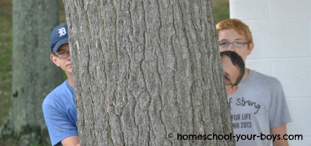 Teenage boys peeking out from behind a tree